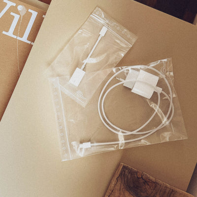 Zwei transparente Plastikbeutel mit verschiedenen weißen elektronischen Kleinteilen und Kabeln, liegend auf einer braunen Kartonoberfläche.