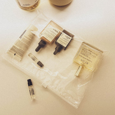 Ein offener, transparenter Plastikbeutel gefüllt mit verschiedenen kleinen Kosmetikproben, darunter Fläschchen mit Pipetten, Tuben und einem Zerstäuber, liegend auf einer hellen, leicht glänzenden Oberfläche.